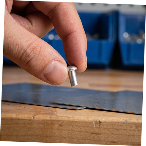 Person holding a solid aluminum dome head rivet above a metal sheet, showcasing the 200 Pcs Solid Aluminum Dome Head Rivets M5x10 for DIY projects.