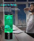 Jellyfish Lamp Liquid Table Lamp With Remote Control Color Changing Night Light For Aquarium Tanks Kid And Adult Friendly Decor Awesome Gift For Christmas And Birthdays placed on desk with green glow and man relaxing nearby.