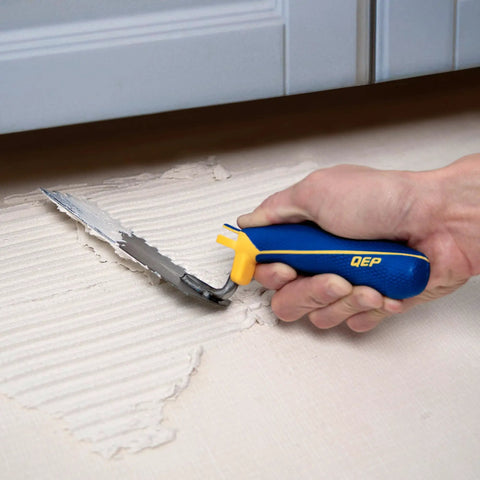 Person using Comfort Grip Square-Notch Margin Tile Trowel With Six-Inch By Two-Inch Blade for thinset application under cabinet.