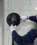 Heavy Duty Electric Drywall Sander With Variable Speed Motor And Hassle Free Vacuum Dust Cleanup For Cleaner Job Sites Plus Dual Bright Led Lamps And Full Sanding Pad Kit For Smooth Finish On Every Home Improvement Project, operator adjusting sander on wall.