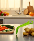 Green spiral vegetable slicer with handle on a kitchen counter beside potatoes and cucumber slices