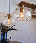 CASAMOTION Glass Pendant Lights, Textured Clear Globe Shade hanging over a kitchen table, featuring a brass socket and black cord.