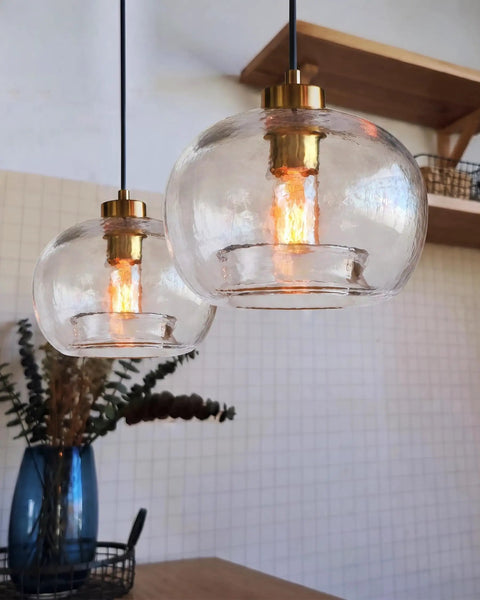 CASAMOTION Glass Pendant Lights, Textured Clear Globe Shade hanging over a kitchen table, featuring a brass socket and black cord.