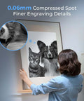 Front view of Creality laser engraver; person hangs large grayscale dog-and-cat print with fur detail inset