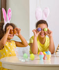 Children wearing bunny ears playing with colorful eggs and 36 pack clear plastic egg cartons with six egg capacity on table.