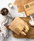 Natural Paper Sandwich Bags With Greaseproof Barrier, 48 Count Pack on table with sandwich and coffee