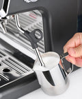 Fully Automatic Espresso Machine With Badass Burr Grinder And Hella Smooth Pulls Featuring Precise Temperature Control Plus Adjustable Milk Frother And Pro Grade 58mm Portafilter For Kitchen Ready Barista Coffee, steam wand in use with milk pitcher.