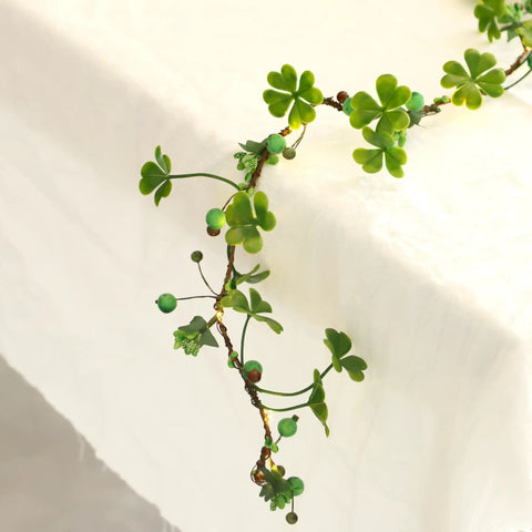 Close-up of green foliage decoration with clover-shaped leaves on a table edge, resembling multicolor daisy fairy lights.