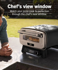 Backyard Pizza Oven With Stone 12 Inch Ready In Just 3 Minutes For Artisan Crusts With 700F Max Temperature Five In One Functionality Bake Broil Proof And Warm Makes Full Family Meals Outdoors For Your Cookout Gray MO201 on patio counter with chef's view window.