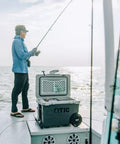 Person fishing on a boat with a 52 Quart Ultra Light Wheeled Cooler Insulated Ice Chest For Beach Camping Fishing Picnics And Boating With All Terrain Wheels Easy Push And Pull Mobility Premium Ice Retention 30 Percent Lighter Than Rotomolded Coolers Olive.