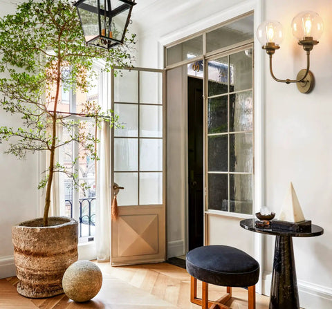 Antique Brass Double Sconce Wall Light With Clear 5.9 Inch Globe Shade in airy living room with glass doors and indoor plant