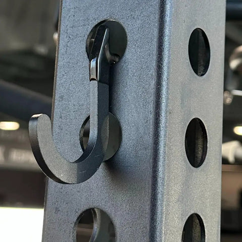 Close-up of black steel hook on power rack for DIY storage, used for hanging gym accessories, fits 1-inch hole-spaced racks.