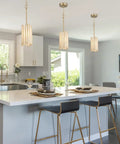 Elegant gold pendant lighting with white glass cylinder illuminates modern kitchen island with dining setup.