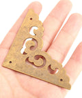 Two Point Five Inch Four Piece Antique Brass Corner Brackets For Furniture Edge Guarding And Vintage Home Decor Makeover featuring a decorative design held in hand.
