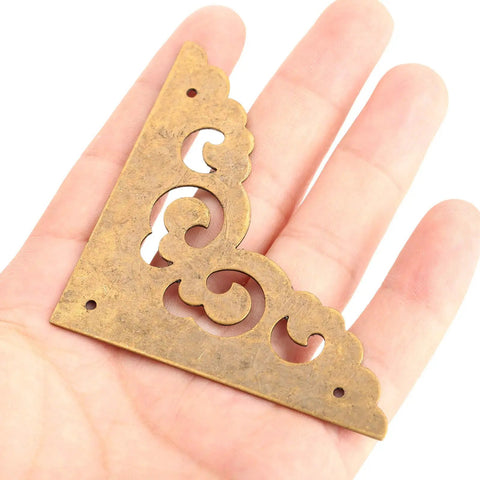Two Point Five Inch Four Piece Antique Brass Corner Brackets For Furniture Edge Guarding And Vintage Home Decor Makeover featuring a decorative design held in hand.
