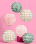 Six Pack Paper Camp Lantern Set In Pink Green And Tan For Bachelorette Parties Birthdays Outdoor Parties And Glamping Decor Includes Two Ten Inch Green Lanterns Two Twelve Inch Tan Lanterns And Two Twelve Inch Pink Lanterns Great For Party Vibes, displayed against pink background.