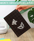 Hand holding Must Have Die Cutting Magnetic Shim Mat Set 6x9 Inch With Card Size Grids And Two Acrylic Cutting Plates For Die Cutting Machines Embossing And Crafting Accessories with metal dies on a grid.