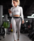 Woman jogging indoors with Hands Free Running Belt For Men And Women Secure Phone Pouch With Key Clip And Essentials Holder Fits 24.5 To 35.5 Inch Waists For Jogging Hiking Cycling Travel And Workouts, wearing white activewear.