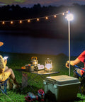 Ultralight Foldable Camping Side Table With Aluminum Build, set up at night by a lake, surrounded by camping gear and lights