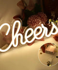 Cheers Neon Sign For Home Bar Wall Decor Battery Or USB Powered Bright Warm White Light Lit For Parties And Bachelorette Celebrations With Home Entertaining Vibe Ultra Lightweight Durable 13 By 5 Inch Sign displayed with USB and battery pack.