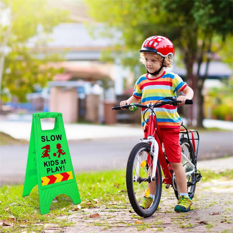 Slow Kids At Play Safety Sign 2 Pack Double Sided Text And Graphics Reflective Tape for street neighborhoods, placed by a child on bike
