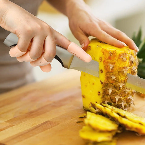 Gel Finger Cots Set 20 Piece Silicone Finger Protectors in use while chopping pineapple on a wooden board.