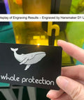 Person holding a laser engraved matte black aluminum business card with whale protection design, created with Hansmaker D1 Ultra.