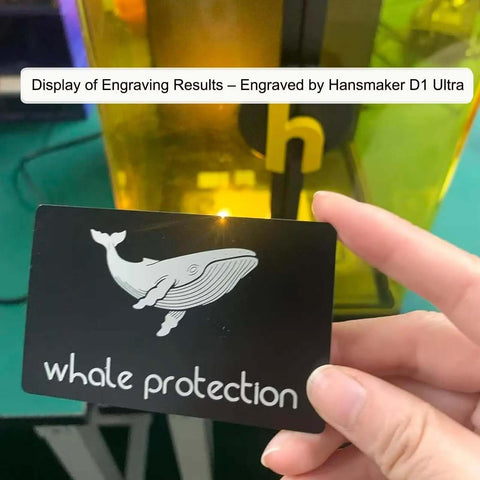 Person holding a laser engraved matte black aluminum business card with whale protection design, created with Hansmaker D1 Ultra.
