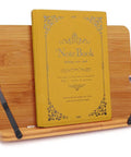 Bamboo Adjustable Book Stand With Tray And Clips, holding a thick notebook, foldable and lightweight, five angle positions.
