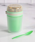 Double Wall Insulated Yogurt Container With Spill Proof For Real Lid Green Snack Cup holding a reusable spoon on a marble surface.