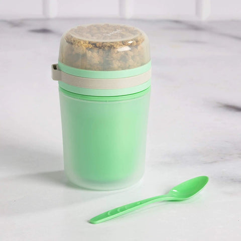 Double Wall Insulated Yogurt Container With Spill Proof For Real Lid Green Snack Cup holding a reusable spoon on a marble surface.