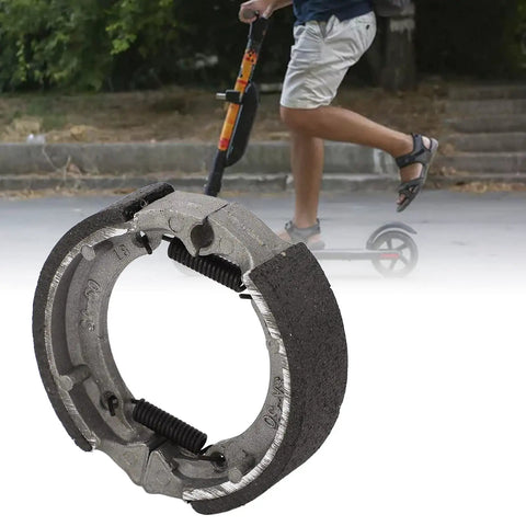 Electric Scooter Front Drum Brake Pad Shoe Replacement Part Built Tough From Lightweight Metal For Smooth Stops And Long Lasting Performance Easy Install Compatible With Most 8 And 9 Inch Models in close-up view with scooter in background.