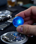 Blue Rubber Ball Watch Case Back Opener For Battery Replacement held above a watch face on a table.