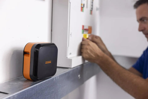 Portable Industrial Label Printer With Bluetooth And Pro Label Tool App Hands Free Belt Clip For Tight Jobsite Spaces Rechargeable Battery Prints Durable Labels Up To 1 Inch Industrial Formats on a metal surface in a worksite.