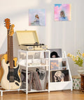 Retro Vinyl Record Player Stand With Adjustable Guitar Holder For Acoustic Or Electric Bass, Huge 150 Album Storage Space, Side Table With Magazine Rack And White Turntable Platform, Cool Vintage Shelf featuring guitars and albums.