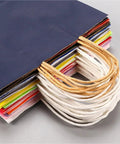 Stack of colorful handle kraft paper bags with sturdy handles for shopping and party packaging, eco friendly 26x12x31cm bags in 50 or 100 pack.