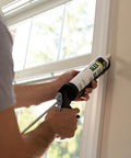 Person applying Painter's Acrylic Latex Caulk White 10.1 Oz All Purpose Sealant For Interior And Exterior Use near a window frame