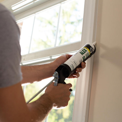 Person applying Painter's Acrylic Latex Caulk White 10.1 Oz All Purpose Sealant For Interior And Exterior Use near a window frame