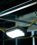 Heavy Duty 100 FT LED String Work Lights X Shaped Uplight hanging from a hook, providing bright illumination in a dark space.