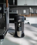 Game Changing Single Dose Coffee Grinder With 64 Millimeter Flat Burrs Stepless Adjustment Heavy Duty Zero Retention Build For Killer Espresso At Home Quiet Compact Design In Crisp White Finish next to an espresso machine.