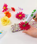 AdTech hot glue gun applying clear adhesive to bright pink flower on floral-pattern clutch.