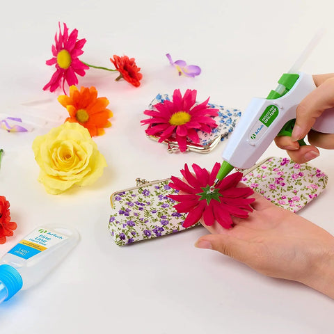AdTech hot glue gun applying clear adhesive to bright pink flower on floral-pattern clutch.
