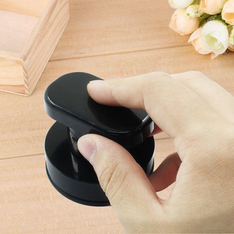 Hand holding 2 Pack Powerful Suction Cup Handles for glass mirrors doors cabinets and bathrooms, black ABS construction on wood surface.