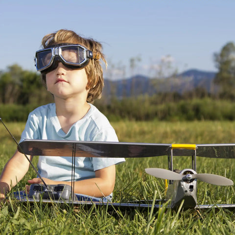 Child sitting on grass with toy airplane, showing two pack 7x6 inch RC propeller set with gray 2 vane blades installed.