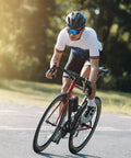 Cyclist riding a road bike on a sunny day, wearing a helmet and sunglasses, showcasing cycling posture and gear.