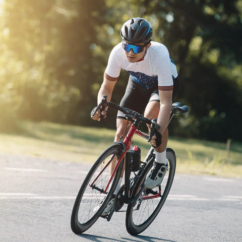 Cyclist riding a road bike on a sunny day, wearing a helmet and sunglasses, showcasing cycling posture and gear.