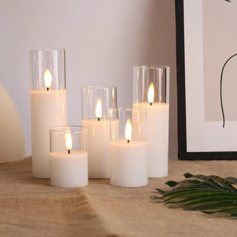Clear Glass Flameless Candles With Remote Set Of 5 Slim Tall LED Pillar Candles on a table with beige cloth and artwork.