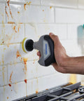 Tackle Stubborn Dirt Effortlessly With This Rechargeable Electric Scrubber Cleaning Kit Featuring Ten Plush Sponge Pads For No Sweat Tile Scouring That Delivers Butter Smooth Shine Across Every Hard Surface At Home. Person using electric scrubber on dirty white tile backsplash.