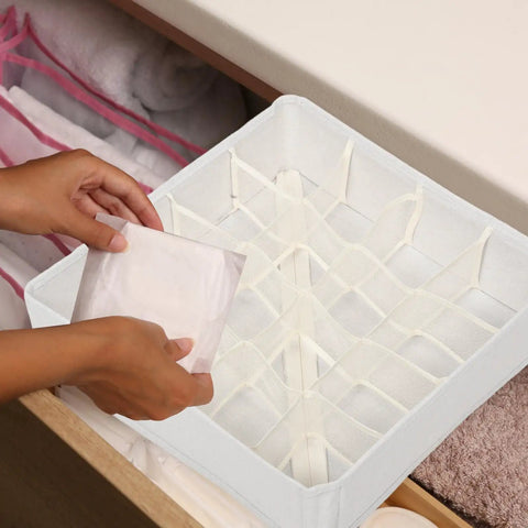 Person placing an item into the Super Slick 16 Compartment Foldable Drawer Storage Box For Underwear And Socks Made From Soft Cotton Linen Blend In Warm Beige.