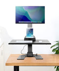 Heavy Duty Electric Standing Desk Converter With Monitor Mount And Wide Keyboard Tray on a wooden table with a displayed monitor.